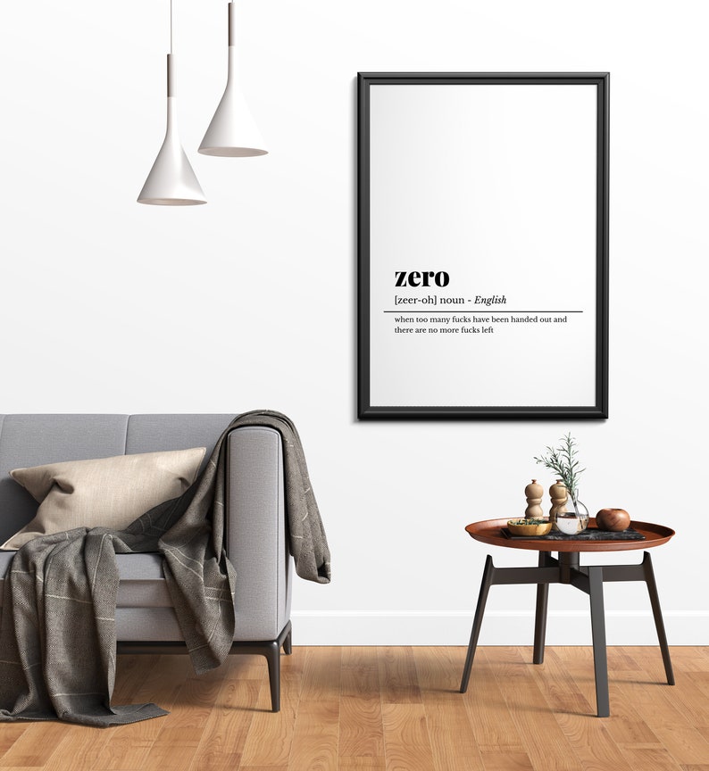 May include: A framed black and white print with the definition of "zero". The print hangs above a gray sofa with a throw blanket and pillow. A small round table with a wooden top and black legs sits nearby.