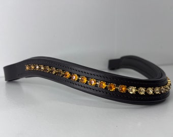 May include: A black leather horse browband, adorned with a line of amber-toned rhinestones. The curved browband features a padded underside. The rhinestones are set in a gold-coloured metal.