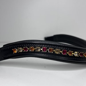 May include: Black leather horse bridle browband with a row of colorful rhinestones in shades of red, orange, and gold. The browband is curved and has a padded design, suitable for equestrian use.
