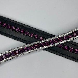 May include: Close-up of a black leather horse bridle with a row of purple and clear crystals. The crystals are set in a silver-coloured metal. The bridle is on a white background.