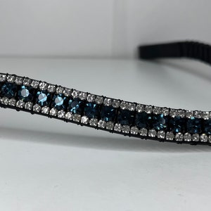 May include: A black headband decorated with rows of shimmering blue and clear crystals. The crystals are set in a silver-toned metal, creating a glamorous accessory. The headband is suitable for various occasions.