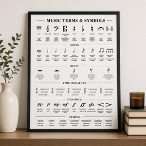 A black-framed poster with white musical terms and symbols, titled "MUSIC TERMS & SYMBOLS," hangs on a light wall.