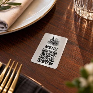 May include: A rectangular silver-toned metal sign featuring a black graphic of a wine bottle and glass at the top, the word MENU in bold capital letters, and a large black and white QR code printed on the lower portion of the surface.