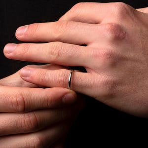 以下が含まれることがあります： 細い銀のバンドリングをした人の手