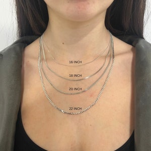 May include: Four silver chain necklaces of different lengths, 16 inches, 18 inches, 20 inches, and 22 inches, are layered on a person's neck.