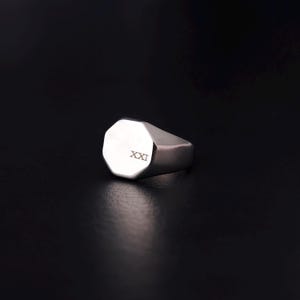 Peut inclure: Une bague chevalière en argent avec une face octogonale. La bague a une finition polie et porte le chiffre romain "XXI" gravé sur la face. La bague est présentée sur un fond sombre.