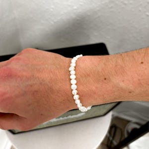 May include: A white pearl bracelet. The bracelet is made of small, round, white pearls strung together. The pearls are uniform in size and shape, creating a delicate and elegant accessory. The bracelet is worn on a wrist.