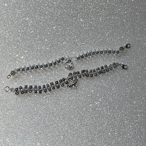 May include: Two silver beaded bracelets with celestial charms. One charm is a crescent moon and the other is a planet with a ring.
