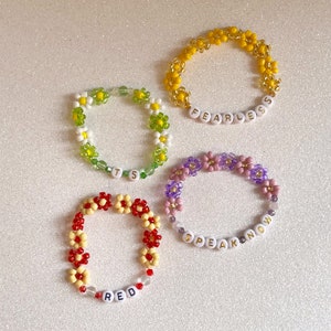 Pu&ograve; includere: Quattro braccialetti di perline con perline a forma di margherita e ciondoli con lettere bianche. I braccialetti compongono le parole "FEARLESS", "SPEAK NOW", "RED" e "ITS".
