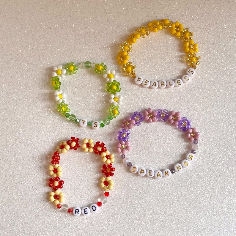 Pu&ograve; includere: Quattro braccialetti di perline con perline a forma di margherita e ciondoli con lettere bianche. I braccialetti compongono le parole "FEARLESS", "SPEAK NOW", "RED" e "ITS".