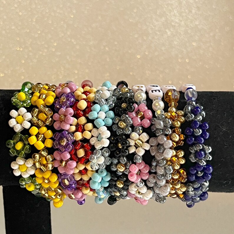 Pu&ograve; includere: Una collezione di braccialetti colorati con perline di diverse forme e colori, tra cui rosa, giallo, blu, verde e nero. I braccialetti sono impilati uno sopra l'altro e sono fatti di piccole perline rotonde.