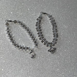 May include: Two beaded bracelets with silver charms. One charm is a crescent moon with a star, the other is a planet with a ring.