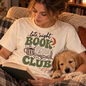 以下が含まれることがあります： 緑色の「late night BOOK CLUB」という文字、開いた本、コーヒーマグ、眼鏡のグラフィックがプリントされたクリーム色の半袖Tシャツ。シャツには「just one more chapter」という文字と小さなハートのアイコンも含まれています。