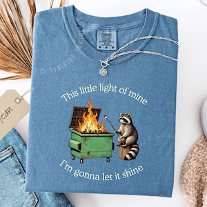 funny dumpster fire shirt, dumpster fire raccoon shirt, raccoon dumpster fire meme tee, trash panda shirt, funny raccoon graphic tee, this little light of mine parody shirt, chaotic raccoon shirt, anxiety humor shirt, funny meme t shirt, roasting marshmallow raccoon tee, comfort colors funny shirt, ironic humor tee, relatable humor shirt, chaos meme shirt, funny animal meme shirt, satirical graphic tee, unhinged raccoon tee, funny gift shirt, mental health meme tee, sarcastic tee, viral shirt