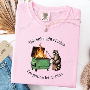 funny dumpster fire shirt, dumpster fire raccoon shirt, raccoon dumpster fire meme tee, trash panda shirt, funny raccoon graphic tee, this little light of mine parody shirt, chaotic raccoon shirt, anxiety humor shirt, funny meme t shirt, roasting marshmallow raccoon tee, comfort colors funny shirt, ironic humor tee, relatable humor shirt, chaos meme shirt, funny animal meme shirt, satirical graphic tee, unhinged raccoon tee, funny gift shirt, mental health meme tee, sarcastic tee, viral shirt