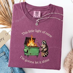 funny dumpster fire shirt, dumpster fire raccoon shirt, raccoon dumpster fire meme tee, trash panda shirt, funny raccoon graphic tee, this little light of mine parody shirt, chaotic raccoon shirt, anxiety humor shirt, funny meme t shirt, roasting marshmallow raccoon tee, comfort colors funny shirt, ironic humor tee, relatable humor shirt, chaos meme shirt, funny animal meme shirt, satirical graphic tee, unhinged raccoon tee, funny gift shirt, mental health meme tee, sarcastic tee, viral shirt