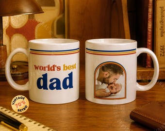 May include: Two white ceramic mugs with a retro design. One mug has the text "world's best dad" in blue and yellow. The other mug features a photo of a father and child. Both mugs have a retro stripe design.