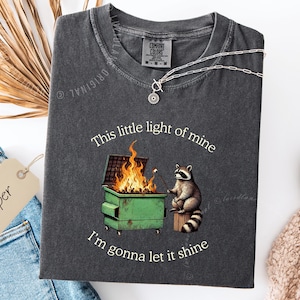 funny dumpster fire shirt, dumpster fire raccoon shirt, raccoon dumpster fire meme tee, trash panda shirt, funny raccoon graphic tee, this little light of mine parody shirt, chaotic raccoon shirt, anxiety humor shirt, funny meme t shirt, roasting marshmallow raccoon tee, comfort colors funny shirt, ironic humor tee, relatable humor shirt, chaos meme shirt, funny animal meme shirt, satirical graphic tee, unhinged raccoon tee, funny gift shirt, mental health meme tee, sarcastic tee, viral shirt