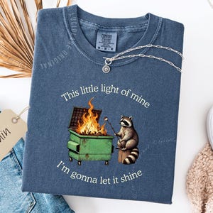 funny dumpster fire shirt, dumpster fire raccoon shirt, raccoon dumpster fire meme tee, trash panda shirt, funny raccoon graphic tee, this little light of mine parody shirt, chaotic raccoon shirt, anxiety humor shirt, funny meme t shirt, roasting marshmallow raccoon tee, comfort colors funny shirt, ironic humor tee, relatable humor shirt, chaos meme shirt, funny animal meme shirt, satirical graphic tee, unhinged raccoon tee, funny gift shirt, mental health meme tee, sarcastic tee, viral shirt