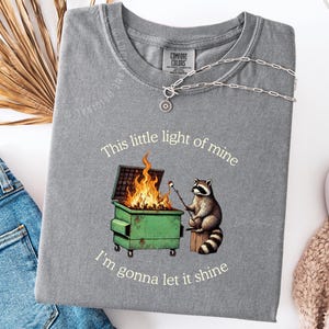 funny dumpster fire shirt, dumpster fire raccoon shirt, raccoon dumpster fire meme tee, trash panda shirt, funny raccoon graphic tee, this little light of mine parody shirt, chaotic raccoon shirt, anxiety humor shirt, funny meme t shirt, roasting marshmallow raccoon tee, comfort colors funny shirt, ironic humor tee, relatable humor shirt, chaos meme shirt, funny animal meme shirt, satirical graphic tee, unhinged raccoon tee, funny gift shirt, mental health meme tee, sarcastic tee, viral shirt