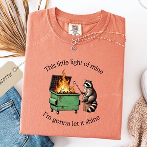 funny dumpster fire shirt, dumpster fire raccoon shirt, raccoon dumpster fire meme tee, trash panda shirt, funny raccoon graphic tee, this little light of mine parody shirt, chaotic raccoon shirt, anxiety humor shirt, funny meme t shirt, roasting marshmallow raccoon tee, comfort colors funny shirt, ironic humor tee, relatable humor shirt, chaos meme shirt, funny animal meme shirt, satirical graphic tee, unhinged raccoon tee, funny gift shirt, mental health meme tee, sarcastic tee, viral shirt