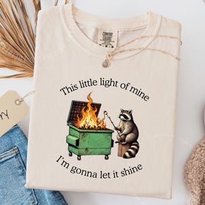 funny dumpster fire shirt, dumpster fire raccoon shirt, raccoon dumpster fire meme tee, trash panda shirt, funny raccoon graphic tee, this little light of mine parody shirt, chaotic raccoon shirt, anxiety humor shirt, funny meme t shirt, roasting marshmallow raccoon tee, comfort colors funny shirt, ironic humor tee, relatable humor shirt, chaos meme shirt, funny animal meme shirt, satirical graphic tee, unhinged raccoon tee, funny gift shirt, mental health meme tee, sarcastic tee, viral shirt