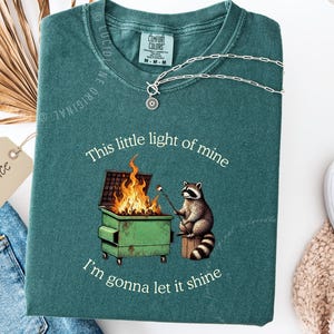 funny dumpster fire shirt, dumpster fire raccoon shirt, raccoon dumpster fire meme tee, trash panda shirt, funny raccoon graphic tee, this little light of mine parody shirt, chaotic raccoon shirt, anxiety humor shirt, funny meme t shirt, roasting marshmallow raccoon tee, comfort colors funny shirt, ironic humor tee, relatable humor shirt, chaos meme shirt, funny animal meme shirt, satirical graphic tee, unhinged raccoon tee, funny gift shirt, mental health meme tee, sarcastic tee, viral shirt