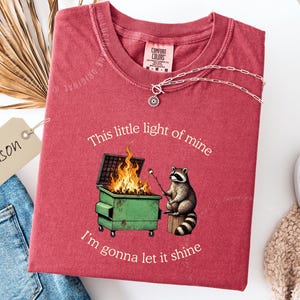 funny dumpster fire shirt, dumpster fire raccoon shirt, raccoon dumpster fire meme tee, trash panda shirt, funny raccoon graphic tee, this little light of mine parody shirt, chaotic raccoon shirt, anxiety humor shirt, funny meme t shirt, roasting marshmallow raccoon tee, comfort colors funny shirt, ironic humor tee, relatable humor shirt, chaos meme shirt, funny animal meme shirt, satirical graphic tee, unhinged raccoon tee, funny gift shirt, mental health meme tee, sarcastic tee, viral shirt