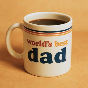May include: A white ceramic coffee mug with a blue and orange striped design. The mug has the text "world's best dad" printed on it.
