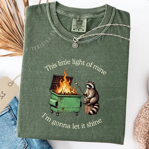 funny dumpster fire shirt, dumpster fire raccoon shirt, raccoon dumpster fire meme tee, trash panda shirt, funny raccoon graphic tee, this little light of mine parody shirt, chaotic raccoon shirt, anxiety humor shirt, funny meme t shirt, roasting marshmallow raccoon tee, comfort colors funny shirt, ironic humor tee, relatable humor shirt, chaos meme shirt, funny animal meme shirt, satirical graphic tee, unhinged raccoon tee, funny gift shirt, mental health meme tee, sarcastic tee, viral shirt