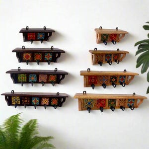 Könnte beinhalten: Eine Sammlung von Holz-Wandregalen mit dekorativen Fliesen-Einsätzen und schwarzen Metallhaken. Die Regale sind in verschiedenen Größen erhältlich und verfügen über farbenfrohe, gemusterte Fliesen in Rot, Blau und Gelb. Jedes Regal hat eine dunkelbraune oder hellbraune Oberfläche.