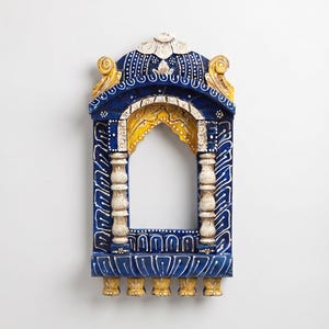 May include: A decorative wooden wall hanging shaped like an arched window frame. It features a deep blue finish with white painted details, yellow accents on the top scrolls and inner arch, and two off-white turned pillars flanking the opening.