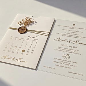 May include: Wedding invitation with a calendar for August 2024, featuring the names "Rodi & Roman". The invitation is adorned with a gold wax seal and dried flowers. The wedding date is August 23rd, 2024. The invitation includes the wedding venue address.