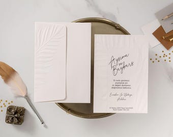 May include: Elegant white invitation suite with embossed leaf design, including an envelope and card with handwritten script. A decorative feather quill and small jeweled box are also present.