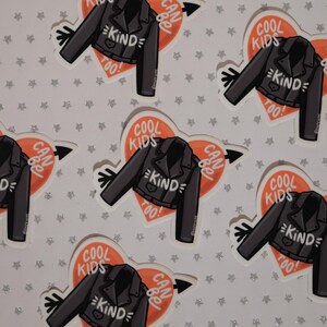 May include: Six stickers with a heart-shaped design featuring a black leather jacket with the text "COOL KIDS CAN BE KIND TOO!" in white. The heart is orange and has a white arrow pointing to the right.