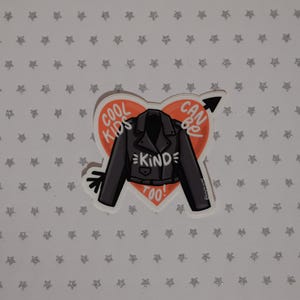 May include: A red heart-shaped sticker with a black leather jacket and the text "Cool Kids Can Be Kind Too!" inside. The sticker is on a white background with silver glitter stars.