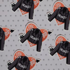 May include: Six stickers with a heart-shaped design featuring a black leather jacket with the text "Cool Kids Can Be Kind Too!" in white lettering. The heart is orange and has a white arrow pointing to the right.