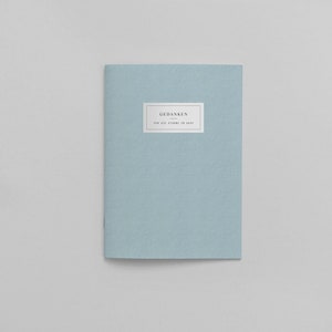 Peut inclure: Un carnet bleu clair avec le texte "GEDANKEN" et "FOR ALL THINGS IN MIND" sur la couverture.