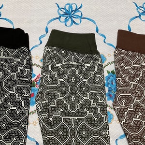 May include: Three pairs of leggings with a geometric pattern in black, brown, and green. The leggings have a white background with a black, brown, or green geometric pattern.