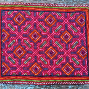 May include: A red, green, orange and blue embroidered fabric with a geometric pattern. The fabric has a black border and a white border.