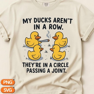 May include: A cream-colored t-shirt featuring a graphic of four yellow rubber ducks in a circle. One duck holds a lit joint with smoke rising. The text reads: MY DUCKS AREN'T IN A ROW. THEY'RE IN A CIRCLE PASSING A JOINT. The shirt has a crew neckline.