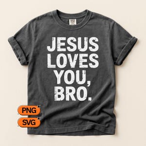 May include: Dark gray t-shirt with the text "JESUS LOVES YOU, BRO." in large, distressed white letters. The shirt has rolled-up sleeves and a classic crew neck. The shirt is a Comfort Colors brand.