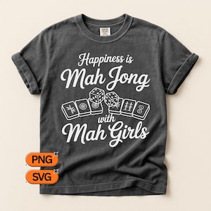May include: Dark gray t-shirt with the text "Happiness is Mah Jong with Mah Girls" in white script. The design includes dice and Mah Jong tiles. The shirt has rolled-up sleeves and a crew neck.