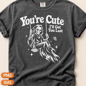 May include: A charcoal grey t-shirt featuring a white graphic of a hooded skeleton sitting on a swing. The text reads You're Cute I'll Get You Last, accompanied by small star and butterfly illustrations. The shirt has a crew neckline and short sleeves.