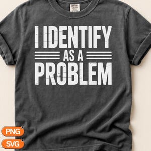 May include: A charcoal gray short-sleeve t-shirt with a crew neckline. The front features white distressed-style text that reads I IDENTIFY AS A PROBLEM with three horizontal lines on each side of the words AS A. The shirt has a Comfort Colors label.