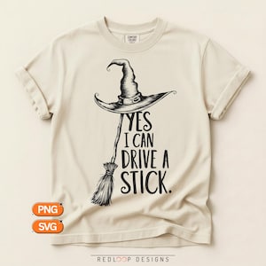 Può includere: Una t-shirt a maniche corte color crema con una grafica nera di un cappello da strega sopra una scopa. Il testo sotto la grafica recita: "YES I CAN DRIVE A STICK." La maglietta ha un girocollo e un'etichetta del marchio Comfort Colors.