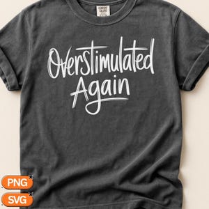 Puede incluir: Una camiseta de manga corta en color gris carbón con el texto blanco "Overstimulated Again" impreso en una fuente estilo pincel en el pecho. La prenda tiene cuello redondo y una etiqueta de la marca Comfort Colors en el interior.