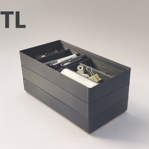 May include: A black, three-tiered, rectangular organizer with compartments for holding office supplies. The organizer is filled with various items, including pens, pencils, paper clips, and a glue stick.