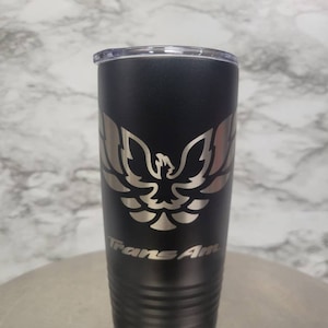 Peut inclure: Un gobelet en acier inoxydable noir avec un logo Trans Am argenté et un motif d'oiseau argenté.