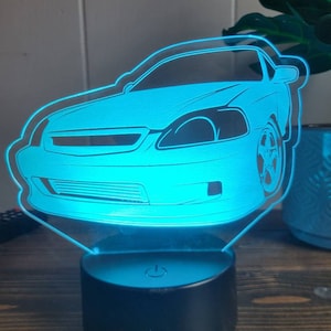 Op de afbeelding: Een blauw acryl nachtlampje in de vorm van een auto. De auto is een Honda Civic met een zwarte basis en een aan/uit-knop aan de zijkant.